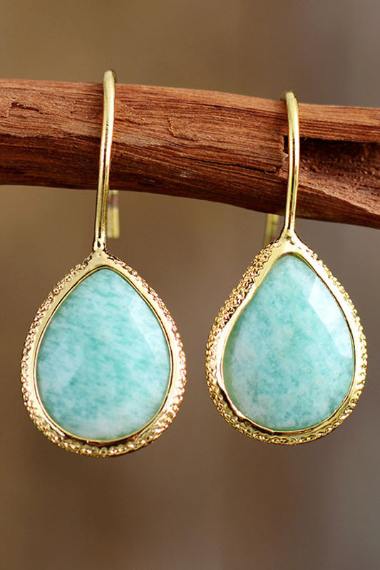 Teardrop-shaped turquoise earrings with gold frames hanging on a wooden stick.
