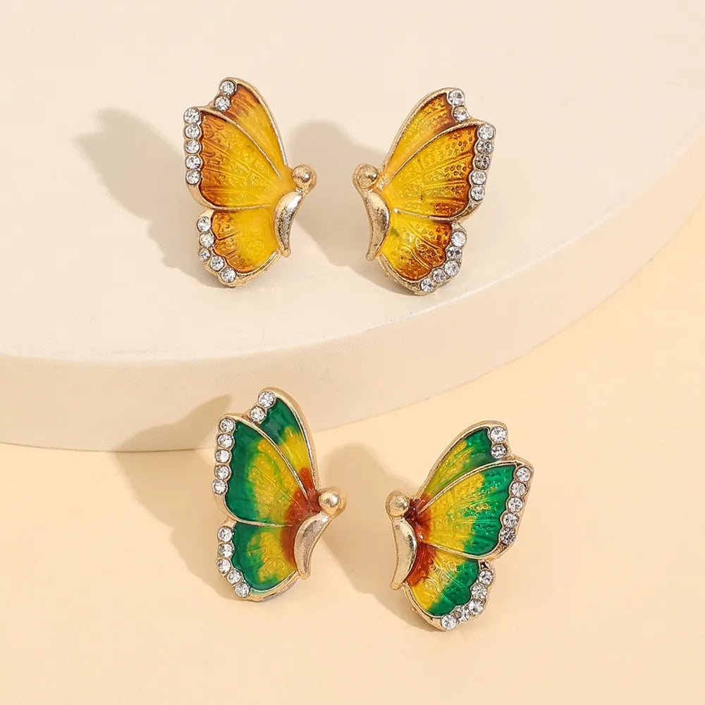Butterfly-shaped earrings with yellow and green wings on a beige background