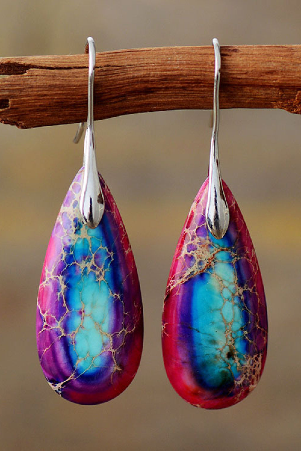 Teardrop-shaped earrings with purple and blue marbled design hanging on a branch.
