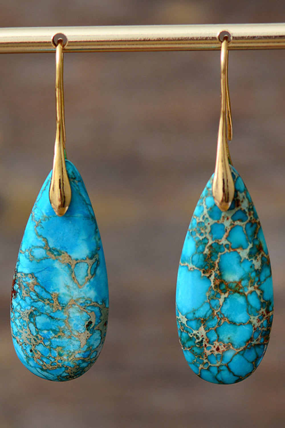 Turquoise teardrop earrings with gold hooks on a blurred background