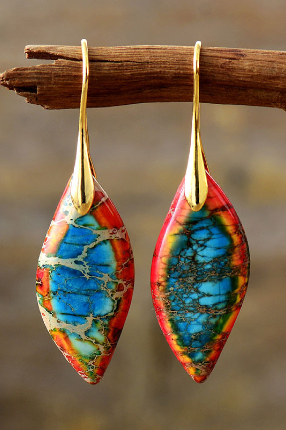 Colorful earrings with gold hooks hanging on a branch against a blurred background