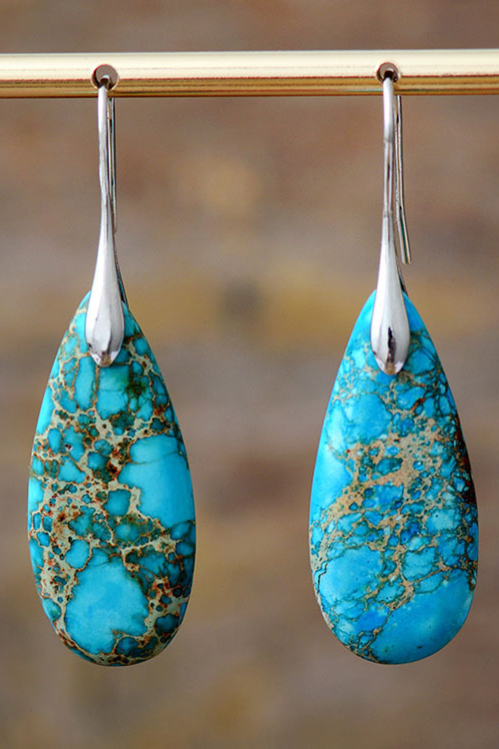 Turquoise teardrop earrings with silver hooks on a blurred natural background
