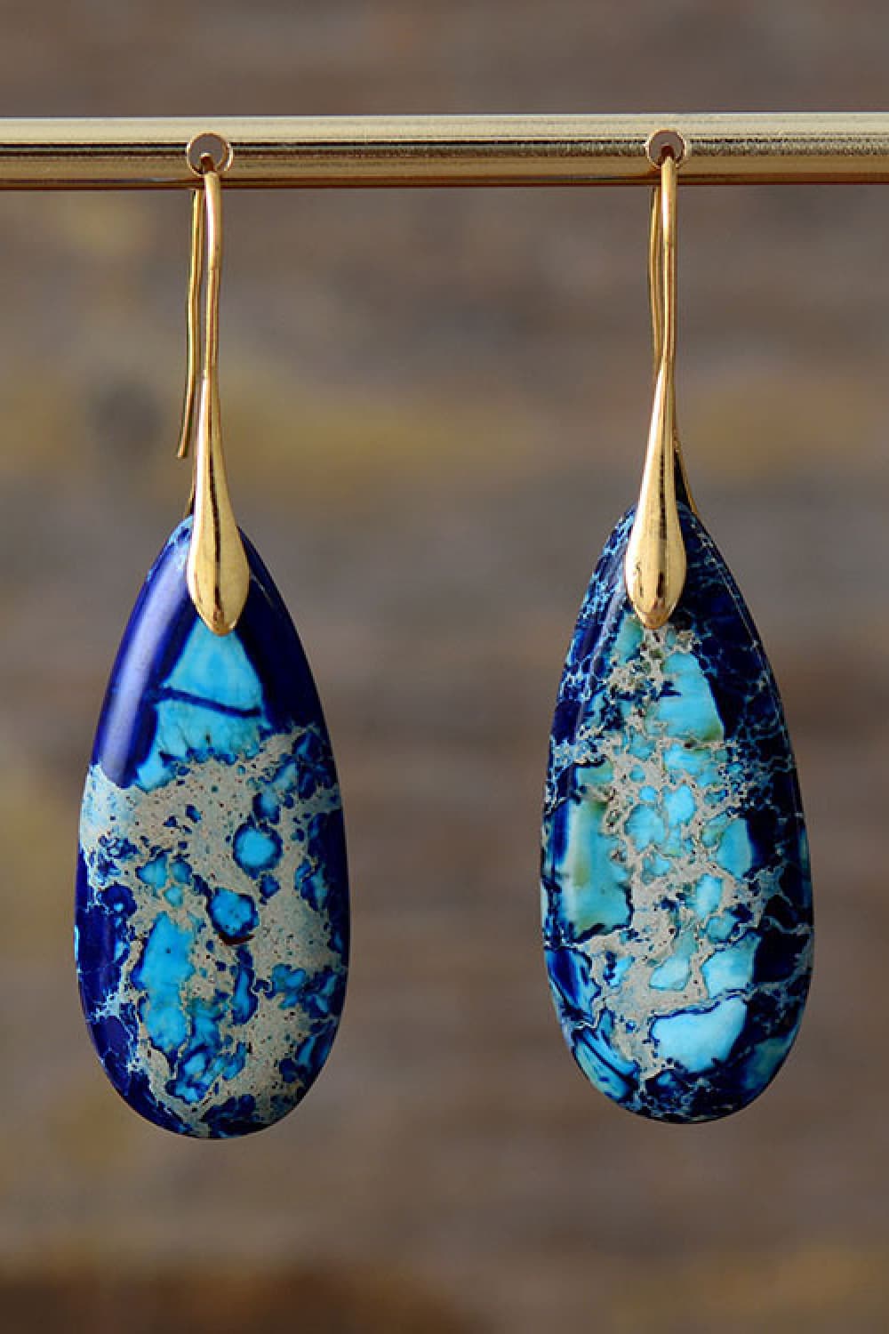Teardrop-shaped blue and gold earrings on a blurred background