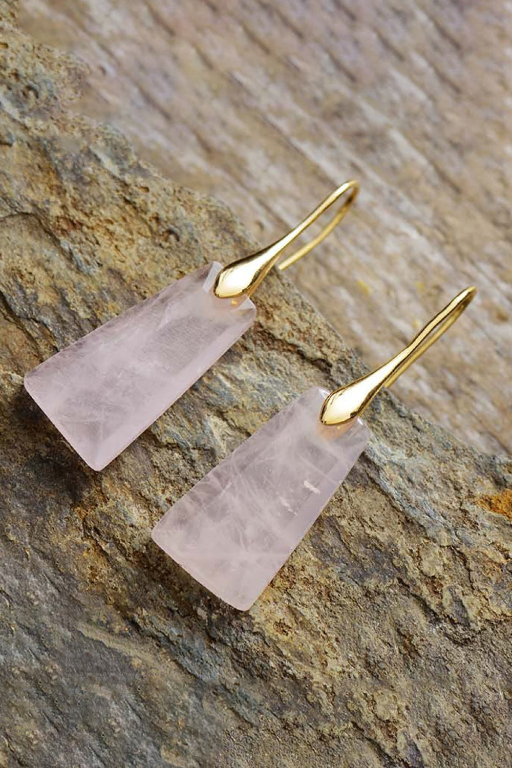Gold earrings with rose quartz stone on a stone surface
