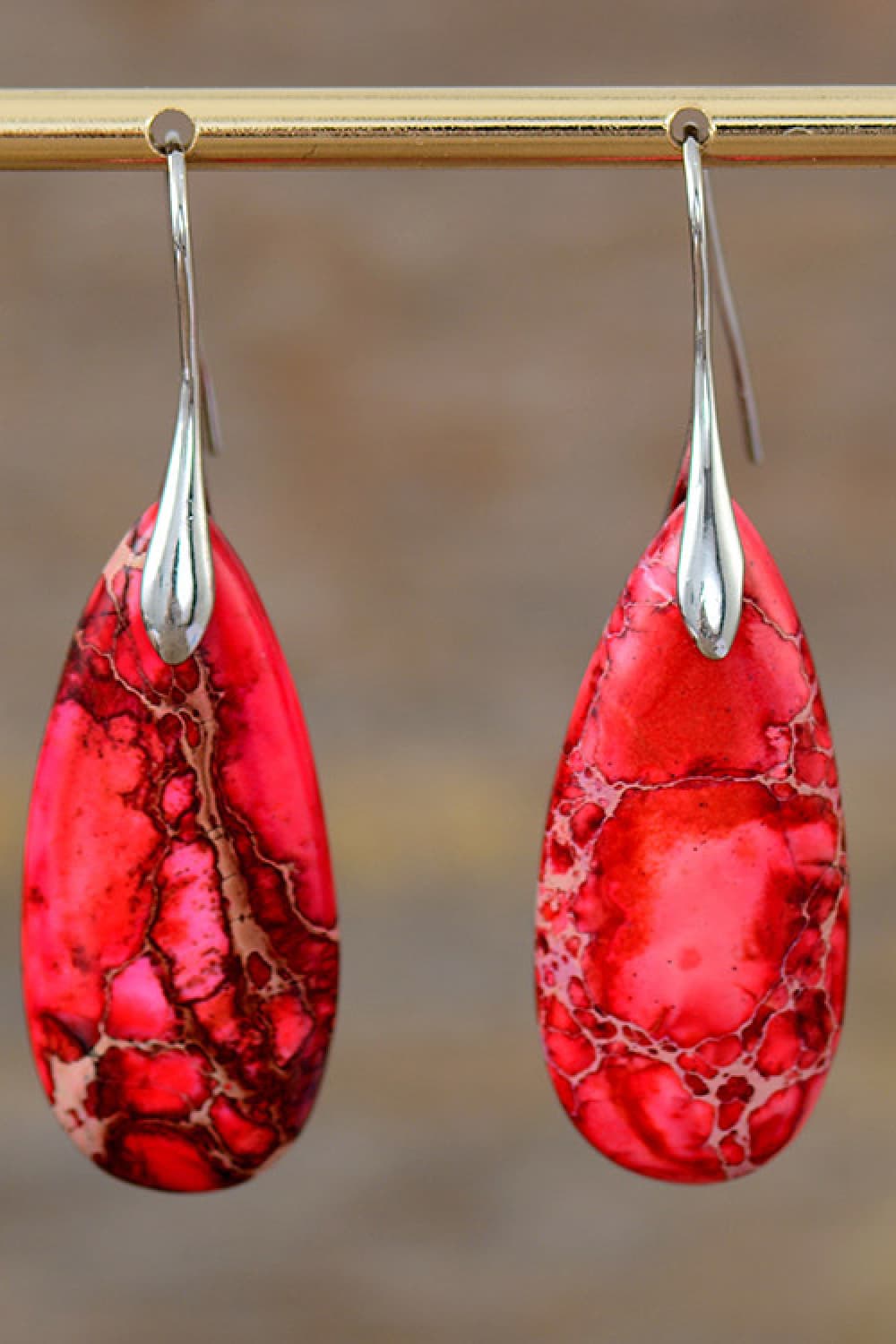 Red teardrop earrings with silver hooks on a blurred background