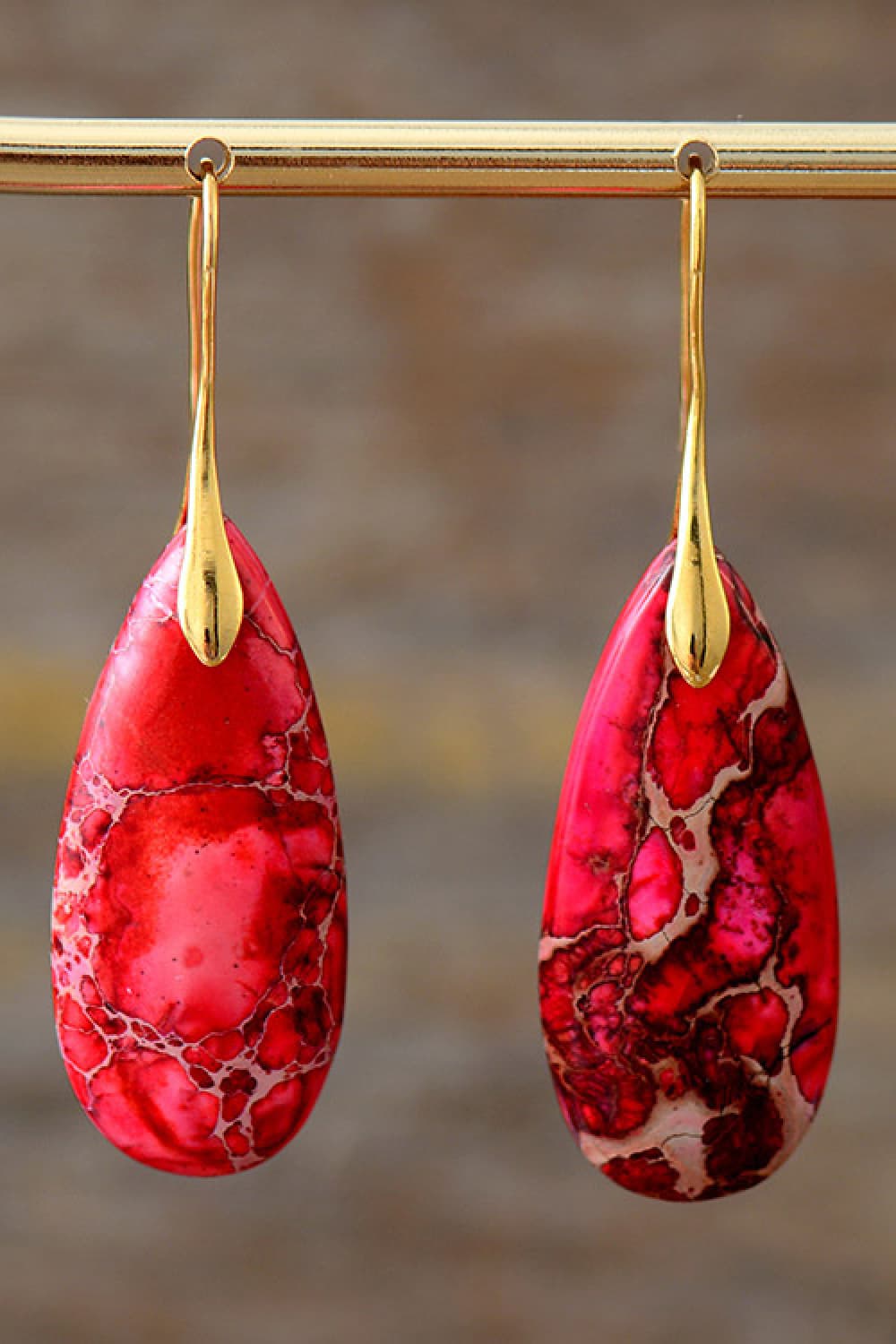 Red teardrop earrings with gold hooks on a blurred background
