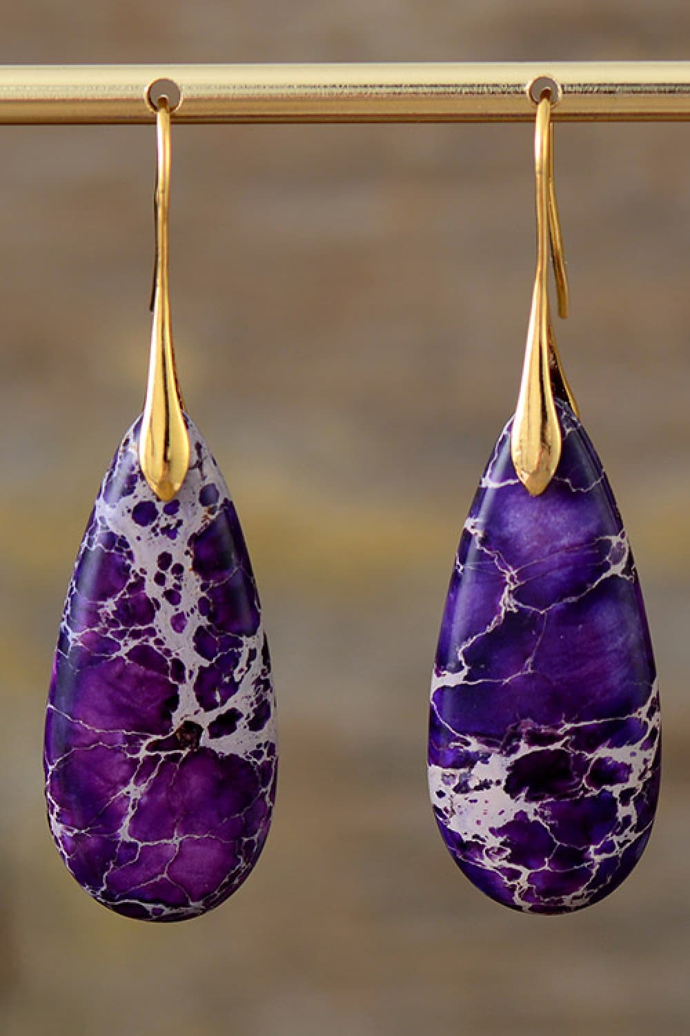 Purple teardrop earrings with gold hooks on a blurred background