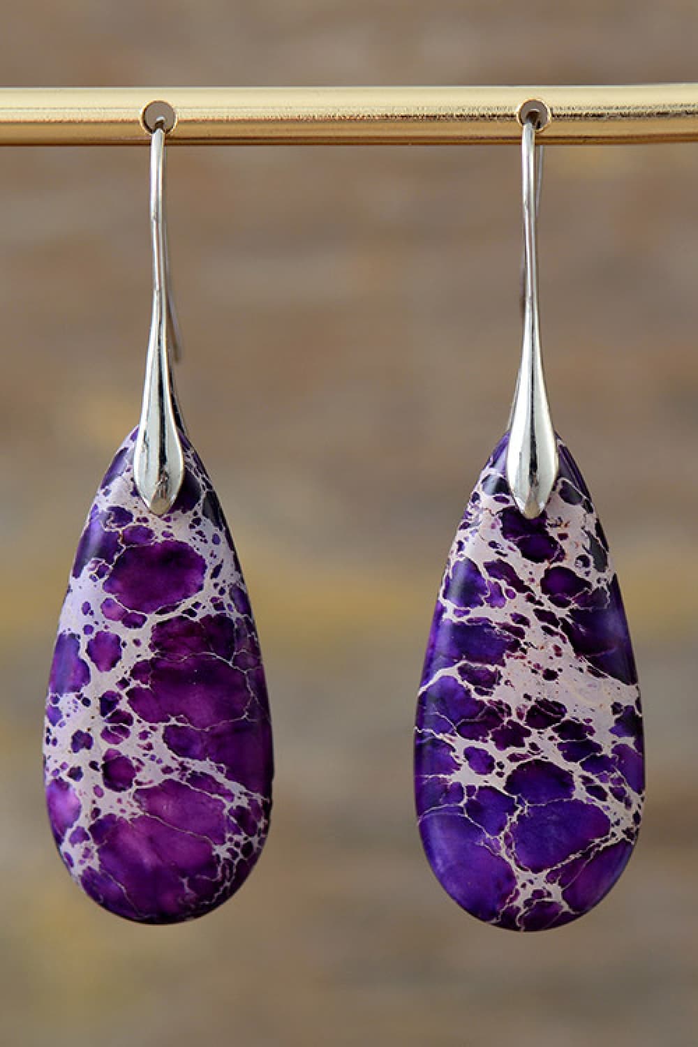 Purple marbled teardrop earrings on a gold earring stand with a blurred background