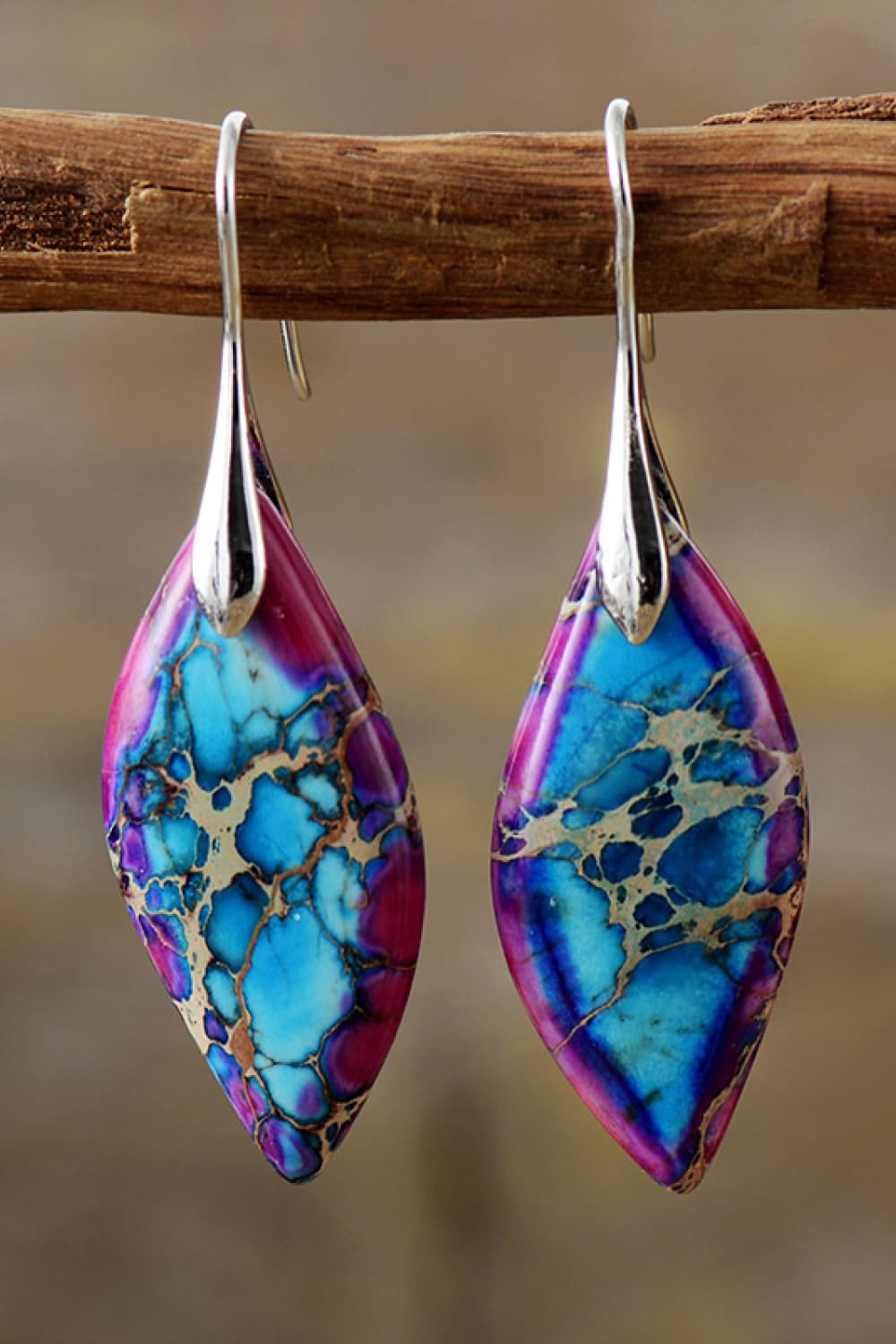Colorful marbled earrings hanging on a wooden stick with a blurred background