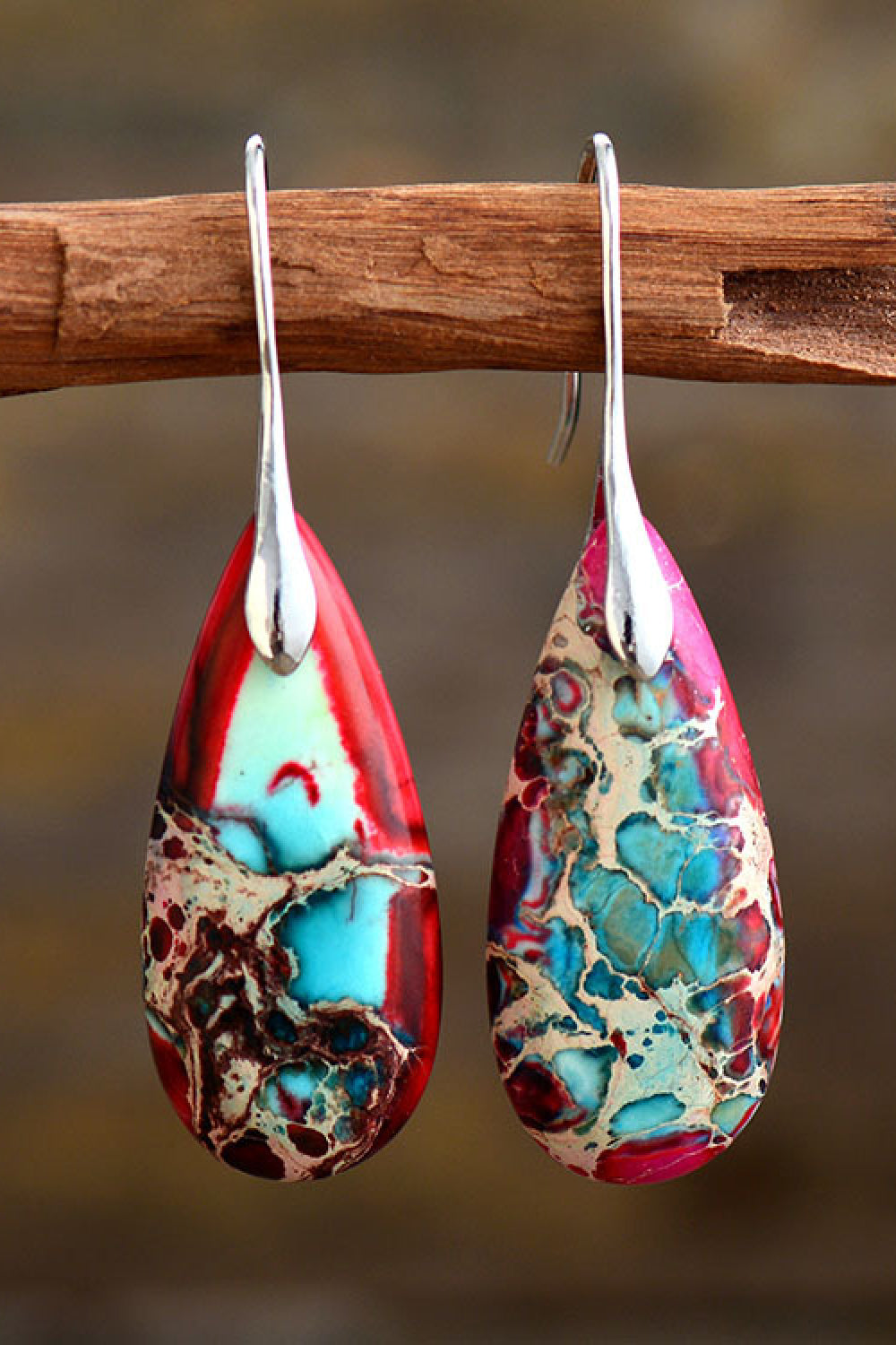 Teardrop-shaped earrings with a marbled design hanging on a wooden stick against a blurred background.