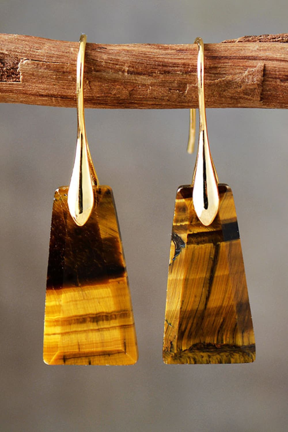 Tiger's eye stone earrings hanging on a wooden stick against a gray background