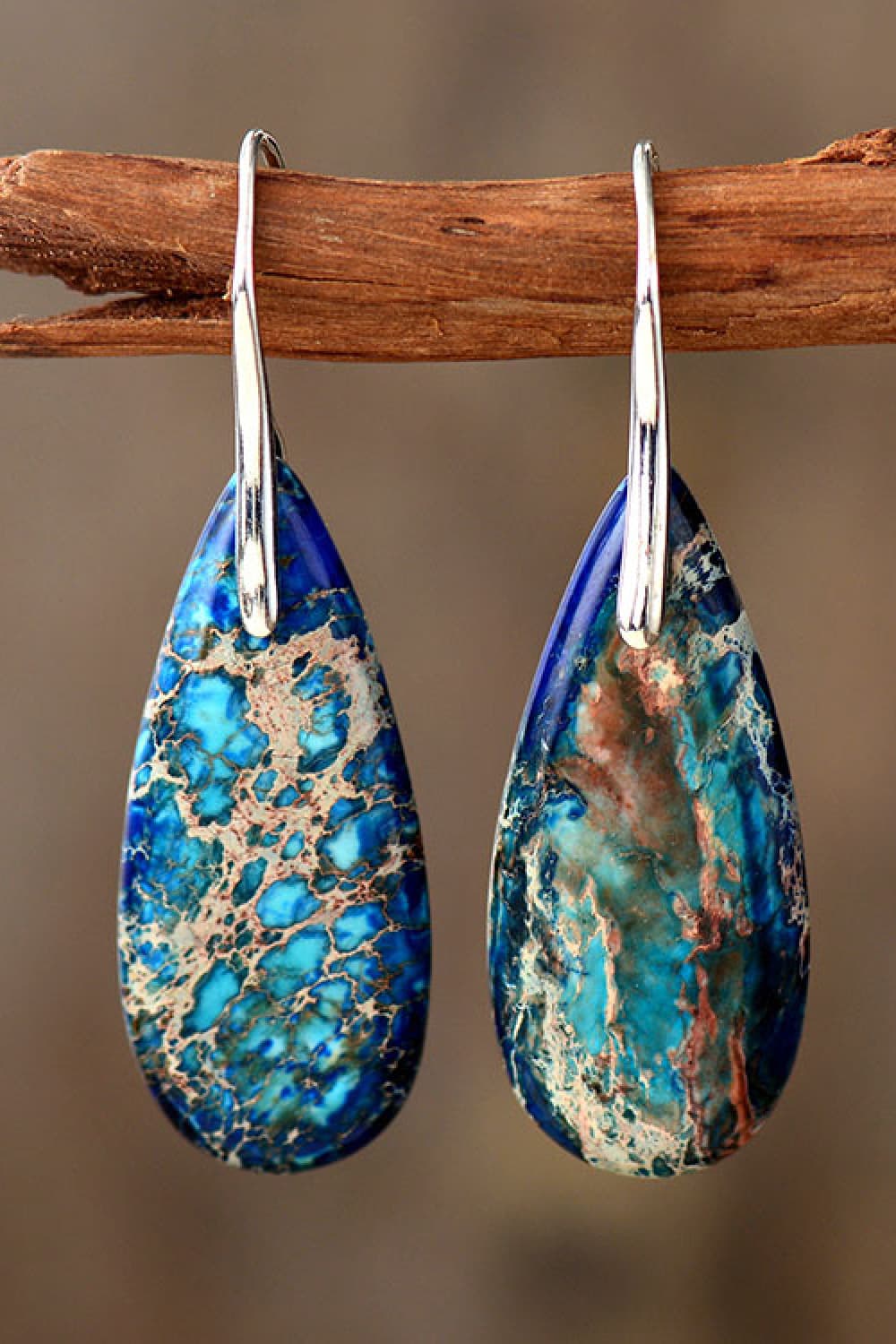Teardrop-shaped blue earrings with a metallic sheen on a wooden branch.